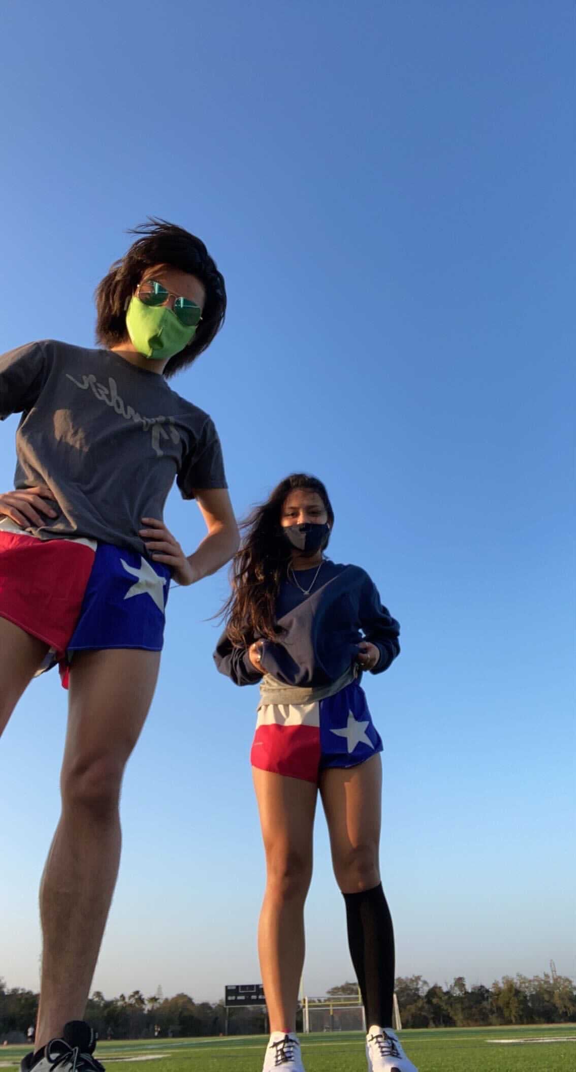 Two athletes wearing Men's Flag 1 Elite Split Shorts in Texas flag design featuring red, white, blue, and star pattern, photographed on a sports field from a low angle against a clear blue sky.