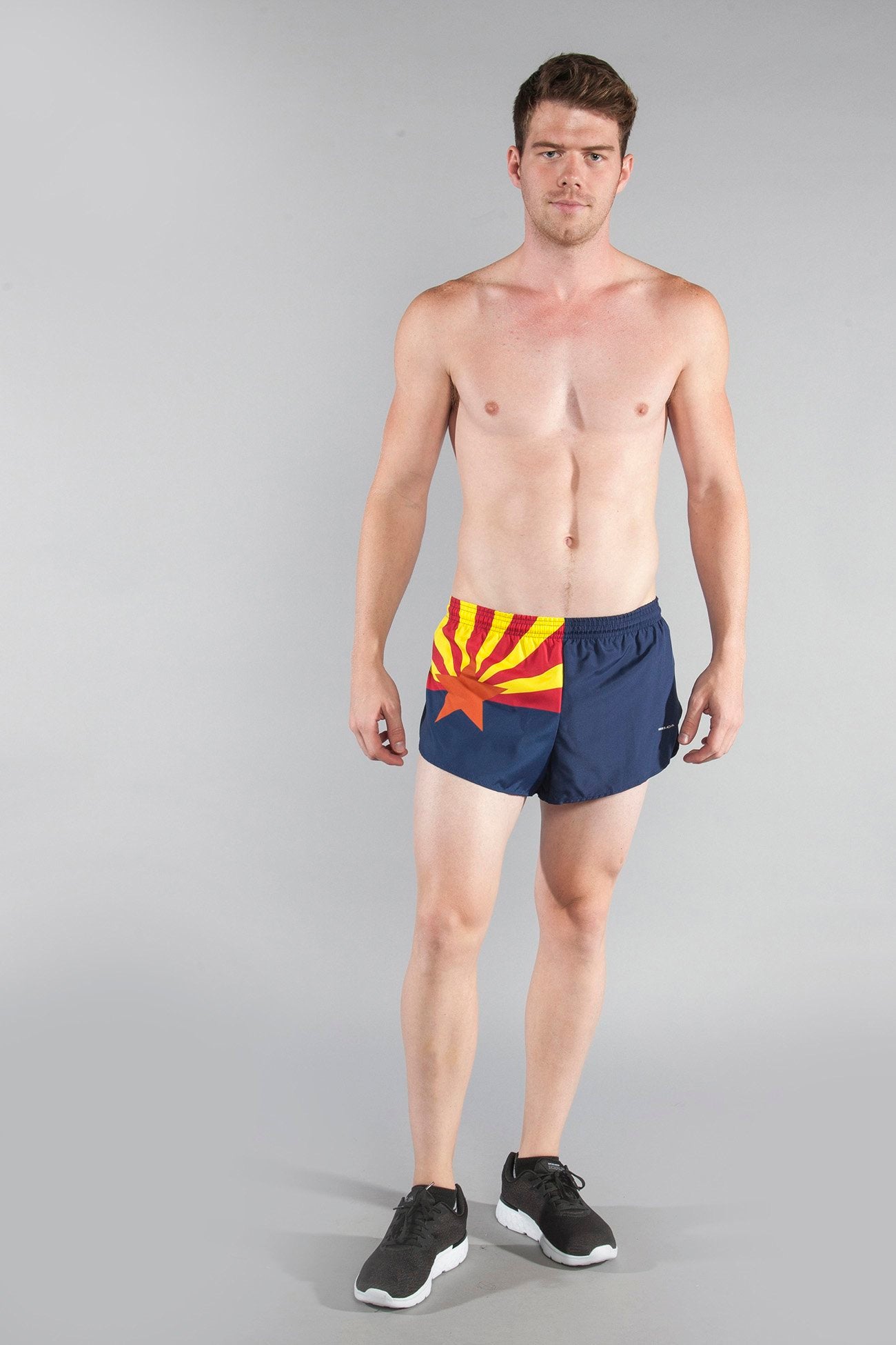 Men's Flag 1" Elite Split Shorts - Arizona, featuring the Arizona state flag design with red and yellow sunburst rays, an orange star, and navy blue lower half, modeled by a shirtless male athlete wearing black sneakers against a gray background.