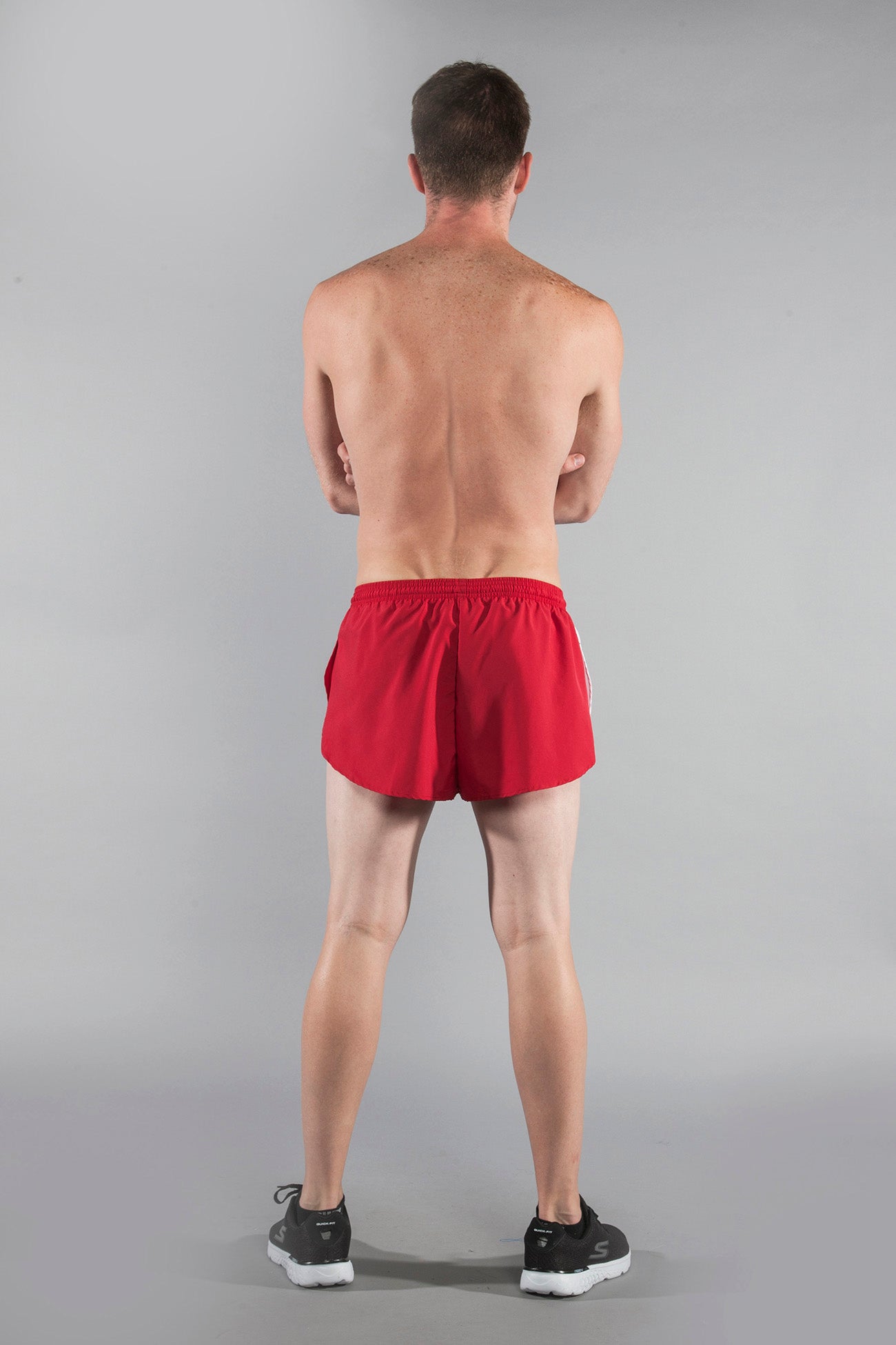 Men's Flag 1" Elite Split Shorts in red with white side stripes, shown from the back on a male model wearing black Skechers sneakers against a grey background.