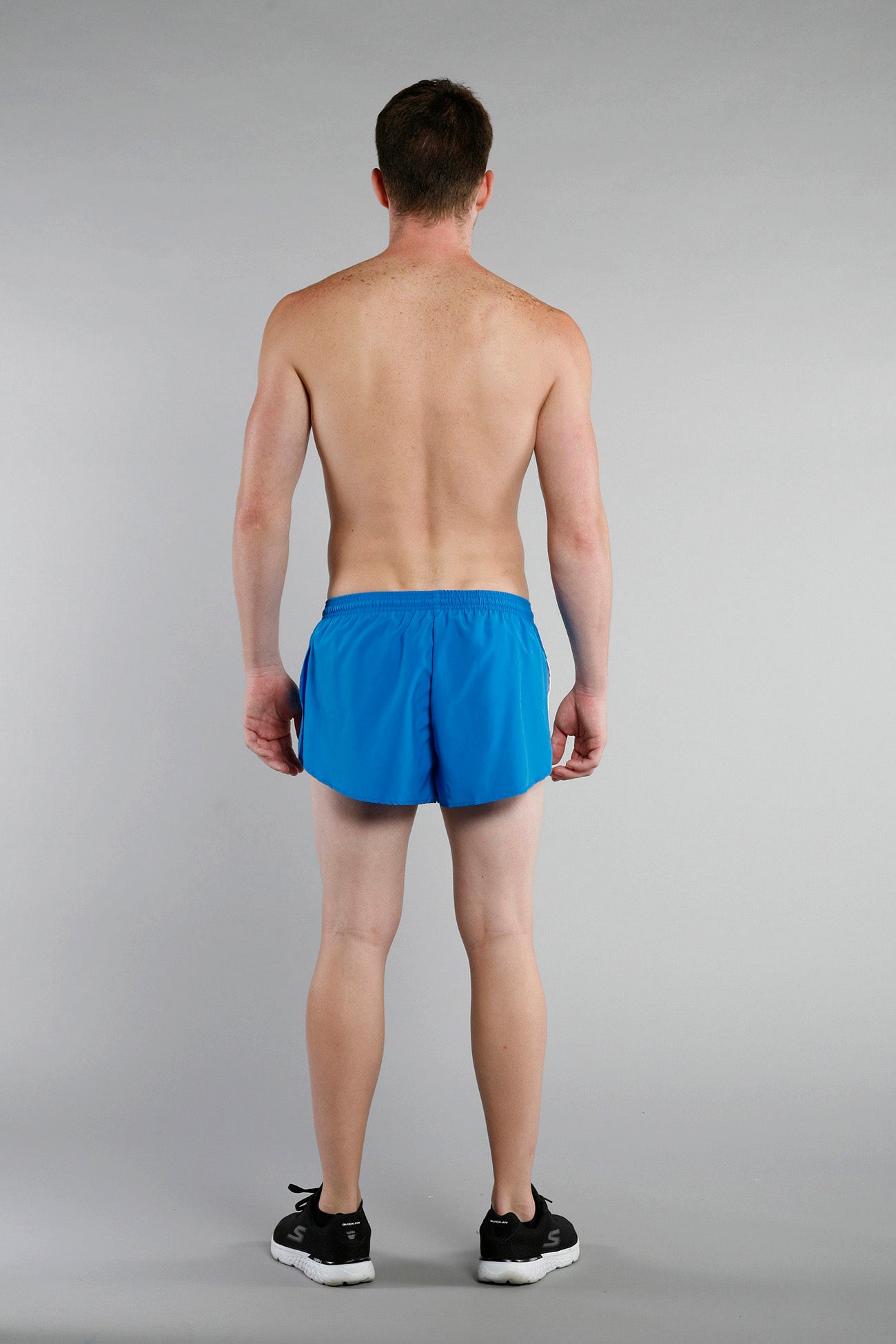 Men's Flag 1" Elite Split Shorts in bright blue with white side stripe, shown from the back on a male model paired with black Skechers sneakers — Chicago colorway.