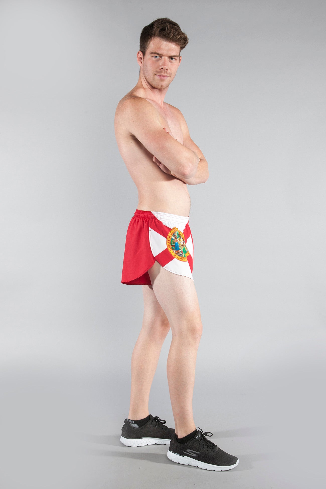 Men's Flag 1" Elite Split Shorts in Florida state flag design, featuring red and white panels with the Florida state seal, modeled by a shirtless man paired with black Skechers sneakers against a gray background.