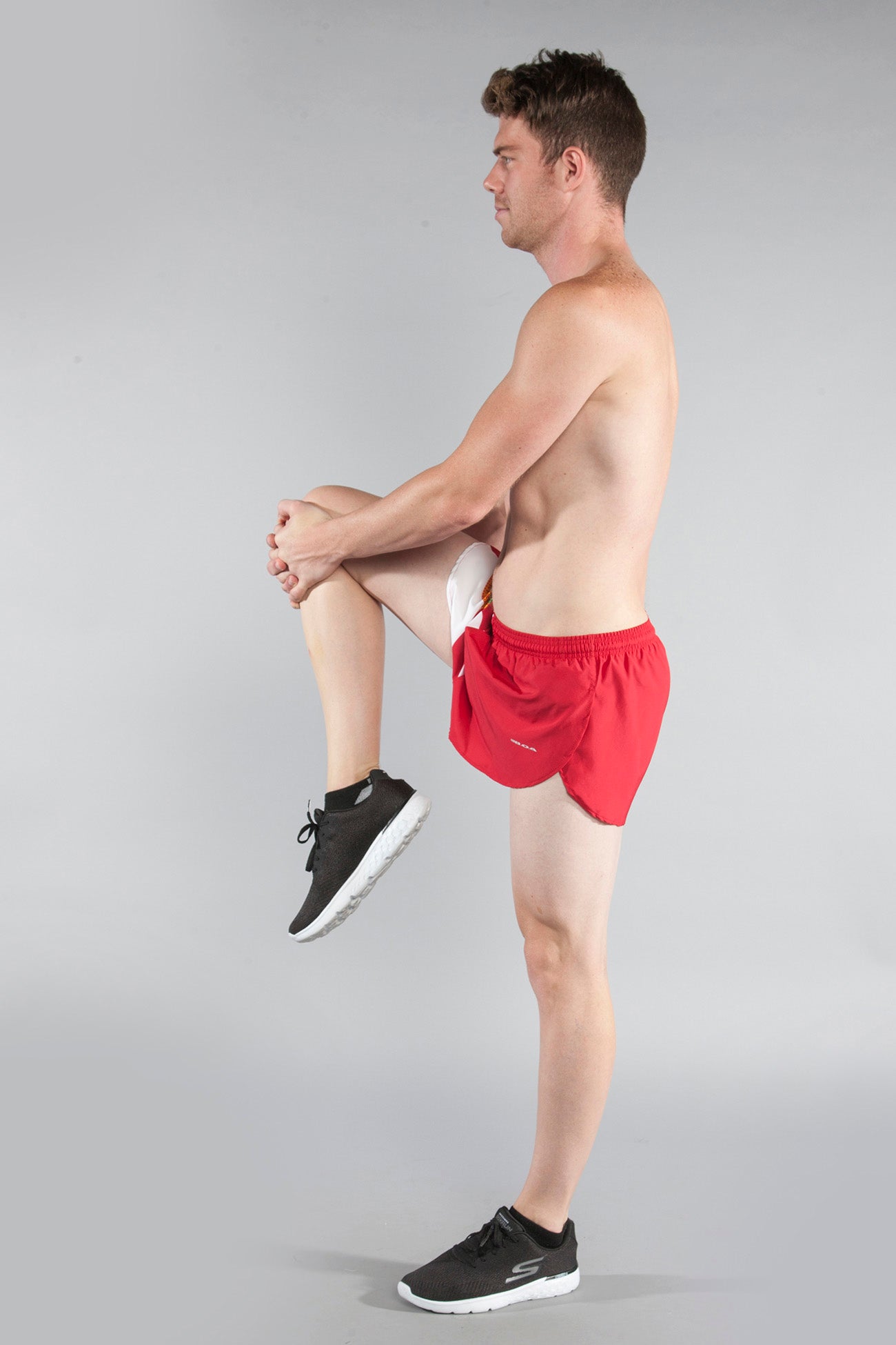 Men's Flag 1" Elite Split Shorts in red with Florida flag design, modeled by a shirtless man performing a standing knee raise stretch, paired with black Skechers sneakers.