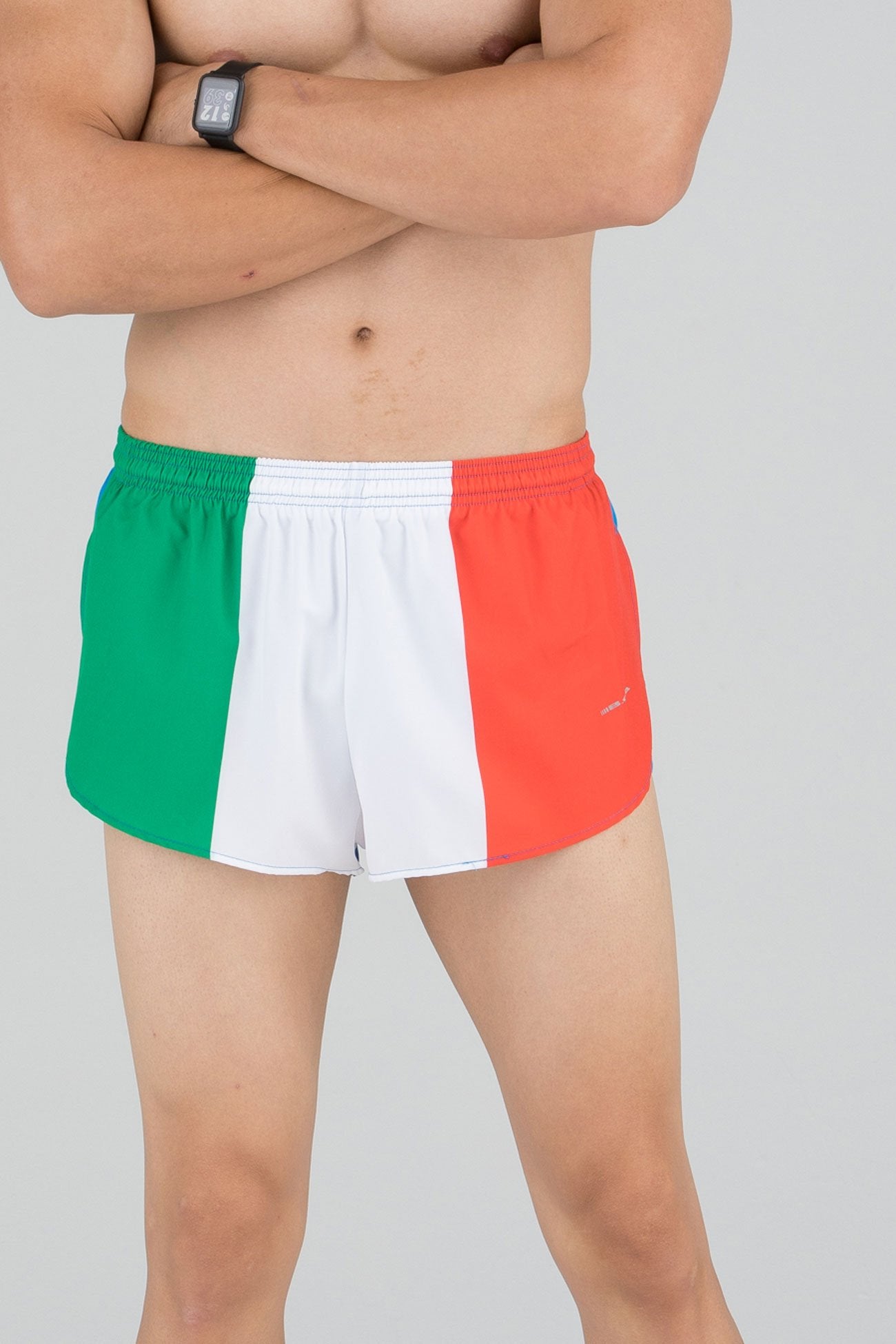 Men's Flag 1" Elite Split Shorts in Ireland flag design featuring bold vertical green, white, and orange stripes with an elastic waistband, modeled by a shirtless male athlete with arms crossed.