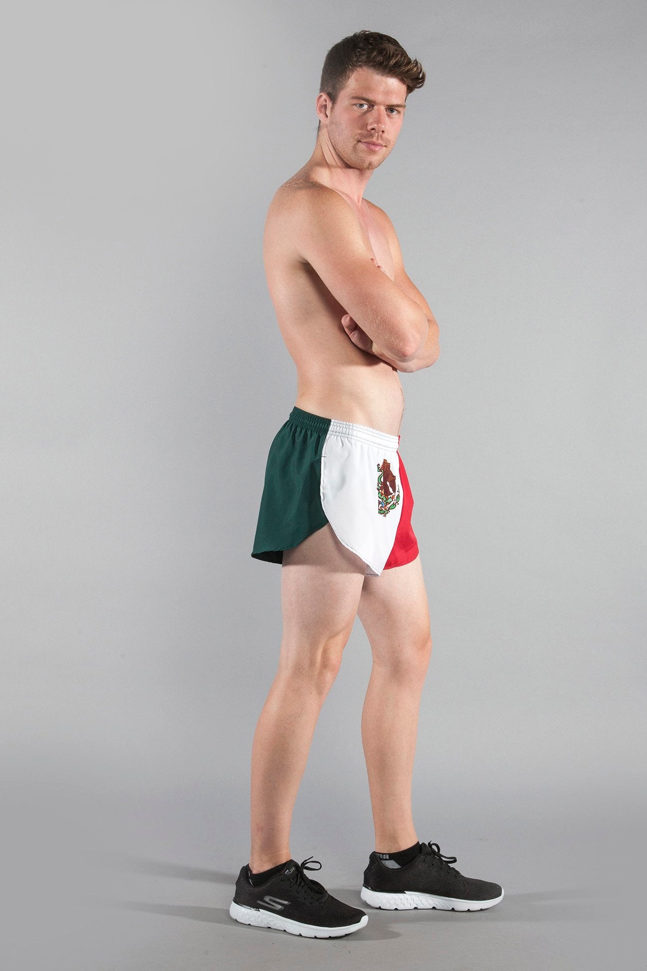 Men's Flag 1" Elite Split Shorts in Mexico flag colors — green, white, and red with the Mexican coat of arms emblem — modeled by a shirtless man wearing black Skechers sneakers against a neutral gray background.