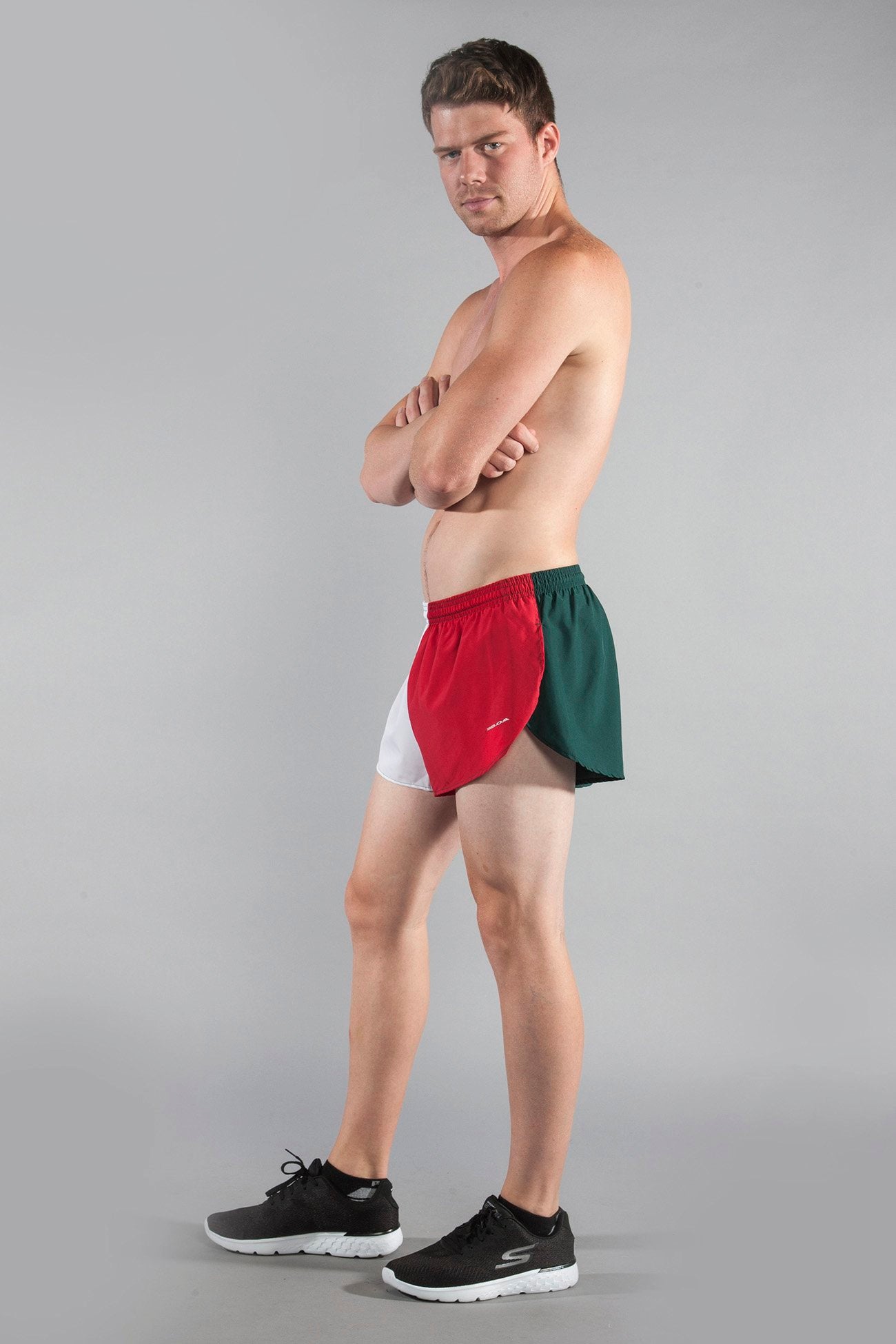 Men's Flag 1" Elite Split Running Shorts in Mexico colorway featuring red, white, and green color-block panels, modeled by a shirtless man paired with black Skechers sneakers against a gray background.